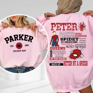 May include: Pink sweatshirt with a graphic design featuring a superhero character, the text "Peter Parker", and the words "Friendly Neighborhood Spidey". The text "Get Knocked Down, Stand Back Up, Protect the People" is also included. The back of the sweatshirt has the text "Parker Est. 2001 Spaider Man" with a spider graphic.