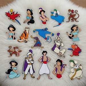 May include: A collection of embroidered patches featuring characters from the animated film Aladdin. The patches include Aladdin, Jasmine, Genie, Abu, Iago, Rajah, and the Magic Carpet, in vibrant colors.