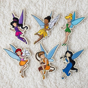 Puede incluir: Seis parches bordados de hadas con alas azules, cada uno con una pose y un atuendo diferentes. Las hadas tienen varios colores de cabello y visten vestidos en tonos morado, amarillo, naranja, verde y azul. Un hada sostiene una pluma y otra una flor.