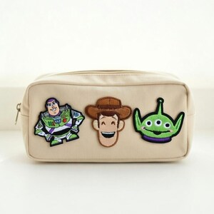Puede incluir: Bolsa de cosm&eacute;ticos rectangular beige con cierre de cremallera. La bolsa presenta parches bordados de Buzz Lightyear, Woody y un personaje alien&iacute;gena verde. Los parches son coloridos y a&ntilde;aden un toque l&uacute;dico a la bolsa.