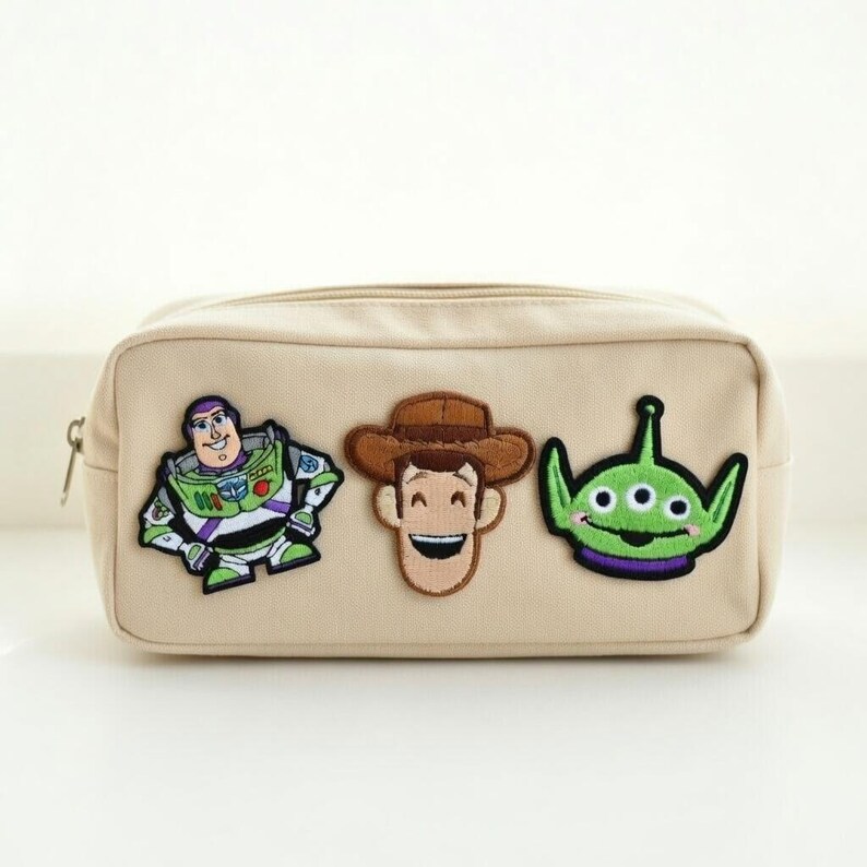Puede incluir: Bolsa de cosm&eacute;ticos rectangular beige con cierre de cremallera. La bolsa presenta parches bordados de Buzz Lightyear, Woody y un personaje alien&iacute;gena verde. Los parches son coloridos y a&ntilde;aden un toque l&uacute;dico a la bolsa.