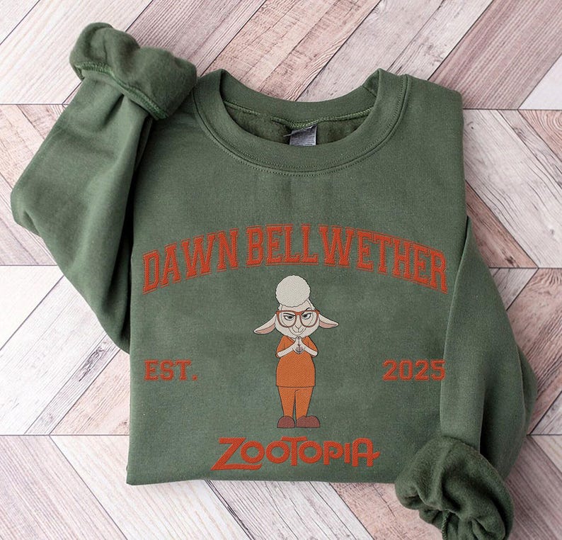 K&ouml;nnte beinhalten: Gr&uuml;nes Sweatshirt mit der Figur Dawn Bellwether aus Zootopia. Das Design umfasst den Text "DAWN BELLWETHER", "EST. 2025" und "ZOOTOPIA" in Orange. Das Sweatshirt hat einen Rundhalsausschnitt und lange &Auml;rmel.