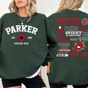 May include: Green sweatshirt with a spider-man theme. The front has the text "Parker Est. 2001 Spaider Man" with a spider graphic. The back has the text "Peter Parker Spidey Get Knocked Down Queens Spider Man Your Ceiling Always Get Bitten By A Spider Back Up".