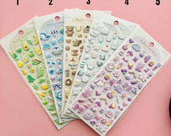 Op de afbeelding: Vijf vellen met kleurrijke, opgeblazen stickers met verschillende ontwerpen, waaronder dieren, voedsel en objecten. De stickers zijn gelabeld met "Puffy Icon Seal" en "Puffy Icon".
