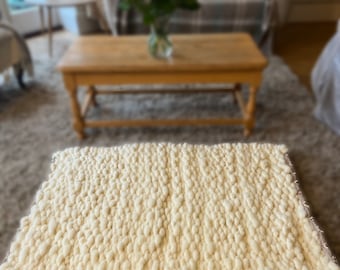 Puede incluir: Una alfombra blanca, esponjosa, tejida a mano con un diseño texturizado y anudado. La alfombra está colocada sobre una alfombra marrón claro en un salón.