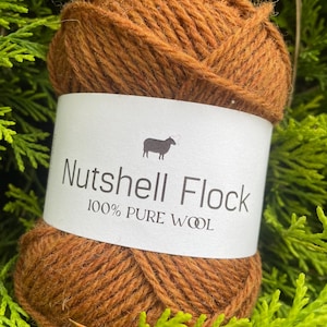 Puede incluir: Una bola de lana marr&oacute;n etiquetada "Nutshell Flock 100% PURE WOOL" con una peque&ntilde;a ilustraci&oacute;n de oveja.