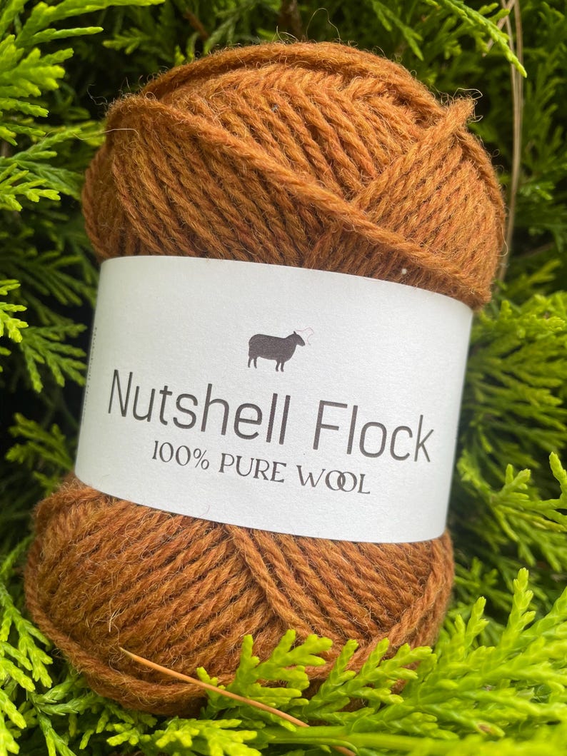 Puede incluir: Una bola de lana marr&oacute;n etiquetada "Nutshell Flock 100% PURE WOOL" con una peque&ntilde;a ilustraci&oacute;n de oveja.