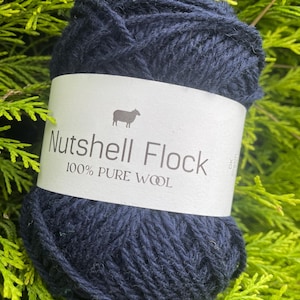 Puede incluir: Una madeja de lana azul oscuro etiquetada "Nutshell Flock 100% Lana Pura" con una peque&ntilde;a ilustraci&oacute;n de oveja.
