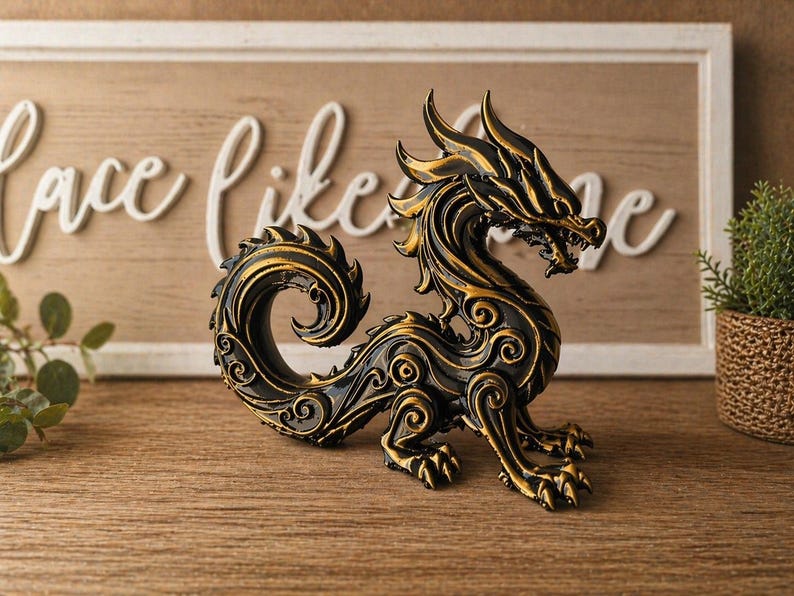 May include: A black and gold dragon figurine with intricate details. The dragon is posed with its head up and tail curled. The figurine is on a wooden surface, with a decorative sign in the background that says "Love Like Me".