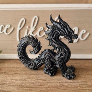 May include: A black dragon figurine with intricate details, including scales, horns, and a curled tail. The dragon is posed on a wooden surface, with a decorative sign in the background.