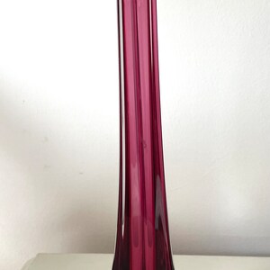 May include: A tall, slender vase with a deep purple hue. The vase has a square base and a narrow opening at the top.