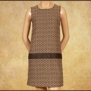 Puede incluir: Un vestido recto sin mangas con un patrón geométrico repetitivo de triángulos en tonos marrón y crema. El vestido incluye una banda horizontal negra sólida en la sección media, un cuello redondo y un dobladillo recto que cae sobre la rodilla.
