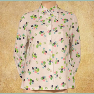 Può includere: Una camicia bianca a maniche lunghe con un colletto grande e un motivo geometrico colorato di cerchi e fiori.