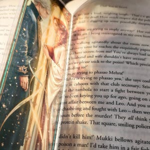 May include: An open book with a detailed illustration of two figures in a romantic scene. The artwork features a man in a dark coat and a woman in a white dress, with a soft, golden glow. Text is visible on the pages.