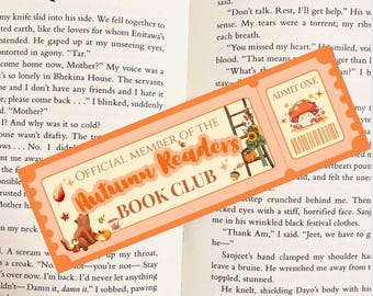 Könnte beinhalten: Ein orangefarbener Lesezeichen mit dem Text "OFFICIAL MEMBER OF THE Autumn Readers BOOK CLUB". Das Lesezeichen zeigt Illustrationen eines Fuchses, Pilze, Blätter und einen Kürbis. Es hat auch ein Ticket mit der Aufschrift "ADMIT ONE".
