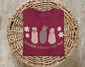 Può includere: Una maglietta color borgogna con una grafica di tre neonati avvolti e il testo "Neonatal Intensive Care Unit".