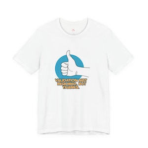 May include: White t-shirt featuring a hand giving a thumbs-up inside a blue circle. The text "VALIDATION NOT REQUIRED, BUT THANKS" is below the graphic in yellow and black. The shirt has a crew neck and short sleeves.