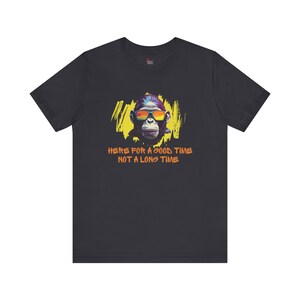 Puede incluir: Camiseta gris oscuro con una ilustración colorida de un mono con gafas de sol. El mono está rodeado de una salpicadura de pintura amarilla y naranja. El texto "HERE FOR A GOOD TIME NOT A LONG TIME" está impreso en naranja debajo del mono.