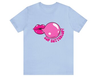 Può includere: Una t-shirt blu chiaro con una grafica di chewing gum rosa e labbra. Il testo "Sup Buttercup?" è stampato in rosa sotto la grafica.