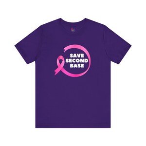 Peut inclure: T-shirt violet avec un ruban rose et le texte "Save Second Base" en blanc.
