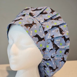 May include: A blue surgical scrub hat with a pattern of black and brown dogs, bones, and tennis balls.