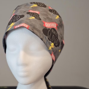 Puede incluir: Un gorro de quirófano gris y negro con un estampado de nubes y rayos. El texto "Certified Black Cloud" está impreso en el gorro.
