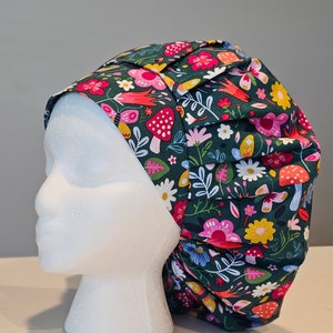 May include: A green scrub hat with a floral and mushroom print. The hat has a gathered top and a wide elastic band.
