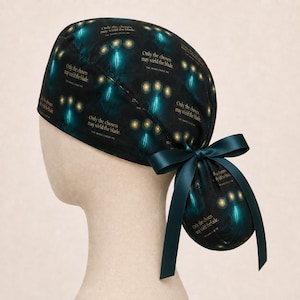 May include: A black scrub cap featuring a repeating pattern of glowing blue sword silhouettes and golden light orbs. The text "Only the chosen may wield the blade" is printed in gold. The cap includes a dark teal ribbon tied into a bow at the back.