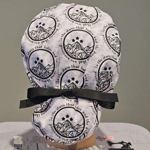 Op de afbeelding: Een witte scrubmuts met een zwart-witte print van een bergketen en sterren. De tekst "Ik heb gedroomd van de sterren die luisteren en de dromen die worden beantwoord" wordt herhaald rond de muts.