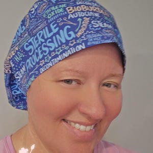 May include: A blue scrub cap featuring a repeating pattern of medical terminology in white and light blue text, including the words Sterile Processing, Bioburden, Autoclave, Decontamination, Steam, and Ethylene Oxide, with small graphic icons.