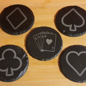 May include: Set of six black slate coasters with different card suit designs: diamond, spade, club, heart, and two playing cards.