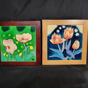 Puede incluir: Dos azulejos de cerámica enmarcados con diseños florales. El azulejo de la izquierda tiene un fondo verde con flores rosas y blancas. El azulejo de la derecha tiene un fondo azul con flores rosas y naranjas.