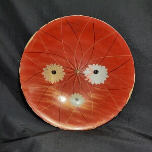 May include: A red wooden bowl with a white and gold floral design. The bowl has a radial pattern of lines radiating from the center.