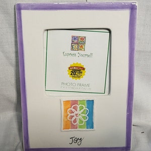 May include: White ceramic photo frame with a purple border. The frame has a 3x3 inch opening and features a colorful flower design with the word "Joy" below it. The frame also includes the text "Express Yourself" and a small sticker that says "Get More Value! Everyday! 20% Off Reg Price".