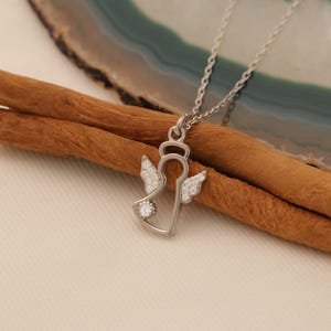 Puede incluir: Un collar de plata con un colgante de &aacute;ngel con detalles de cristal transparente. El colgante tiene forma de &aacute;ngel con alas y halo. El collar est&aacute; en una cadena de plata.