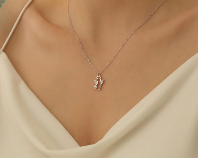 Puede incluir: Un collar de plata con un delicado colgante de &aacute;ngel con peque&ntilde;as piedras transparentes. El colgante es un simple contorno de un &aacute;ngel con alas.