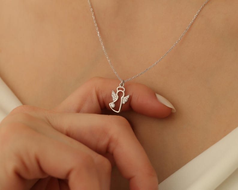 Puede incluir: Un collar de plata con un peque&ntilde;o colgante de &aacute;ngel con una sola piedra transparente en el centro. El &aacute;ngel tiene alas y un halo.