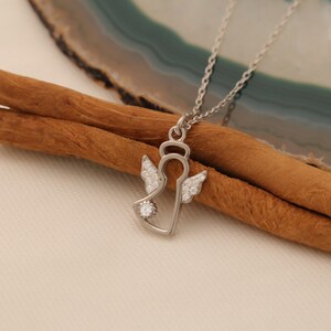 Puede incluir: Un collar de plata con un colgante de &aacute;ngel con detalles de cristal transparente. El colgante tiene forma de &aacute;ngel con alas y halo. El collar est&aacute; en una cadena de plata.