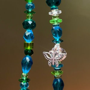 May include: Two beaded necklaces with a butterfly charm. The beads are green, blue, and clear. The butterfly charm is silver.