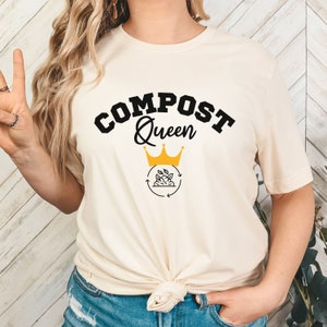 May include: A white t-shirt with the text "COMPOST Queen" in black lettering. A gold crown sits above the text, and a black and white illustration of a compost bin with leaves and arrows is below the crown.