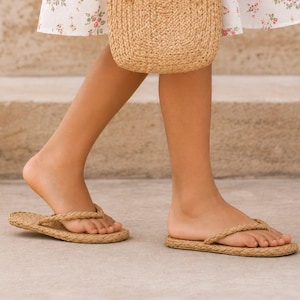 May include: A woven straw handbag with two rounded handles and a pair of matching woven straw flip-flops. The handbag features a textured, natural tan finish, while the flip-flops have a braided strap design and a flat, woven straw sole.