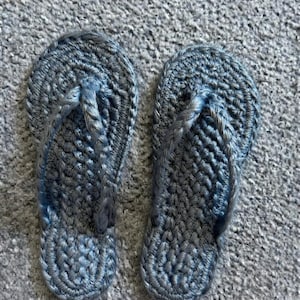 May include: A pair of slate blue flip-flops crafted from thick, braided cord material. The footwear features a rounded toe bed and a Y-shaped strap design, both constructed with a consistent, textured crochet-like weave pattern throughout.