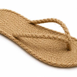 May include: A single flip-flop sandal constructed entirely from tan-colored braided rope. The flat sole features a coiled rope design, while the Y-shaped toe post strap is made from a matching twisted rope material, creating a textured appearance.