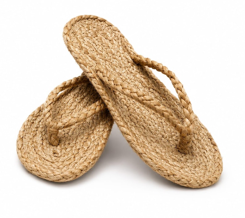 May include: A pair of tan flip-flops constructed from braided natural fiber rope. The footwear features a flat, oval-shaped sole and a braided thong strap that connects to the center of the sole, showcasing a consistent woven texture throughout.