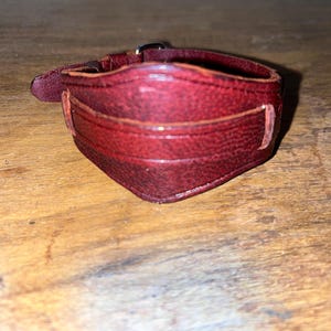 May include: A dark red leather bracelet with a buckle fastening.