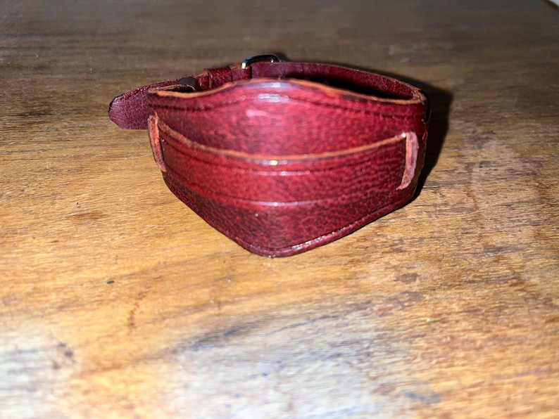 May include: A dark red leather bracelet with a buckle fastening.