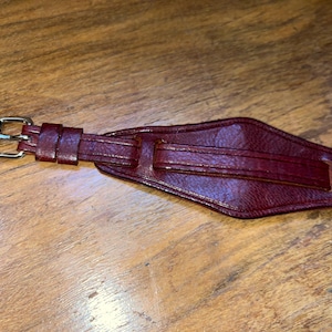 May include: A dark red leather watch strap with a silver buckle.