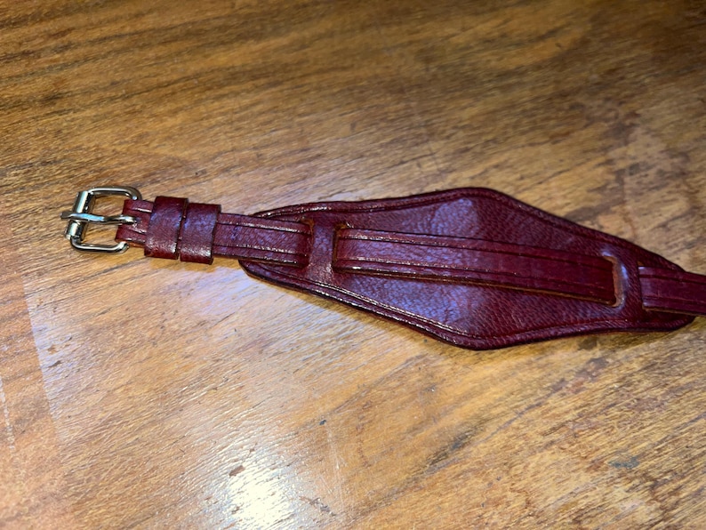 May include: A dark red leather watch strap with a silver buckle.