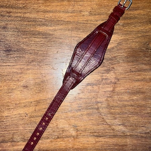 May include: A dark red leather watch strap with a silver buckle. The strap is designed with a unique, diamond-shaped section in the middle.