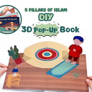 Peut inclure: Un livre pop-up 3D de bricolage intitulé "5 Pillars of Islam". Le livre ouvert révèle une illustration colorée d'un tapis de prière, une figurine en rouge et une petite table avec une lampe. Un petit livre est montré en haut à gauche.